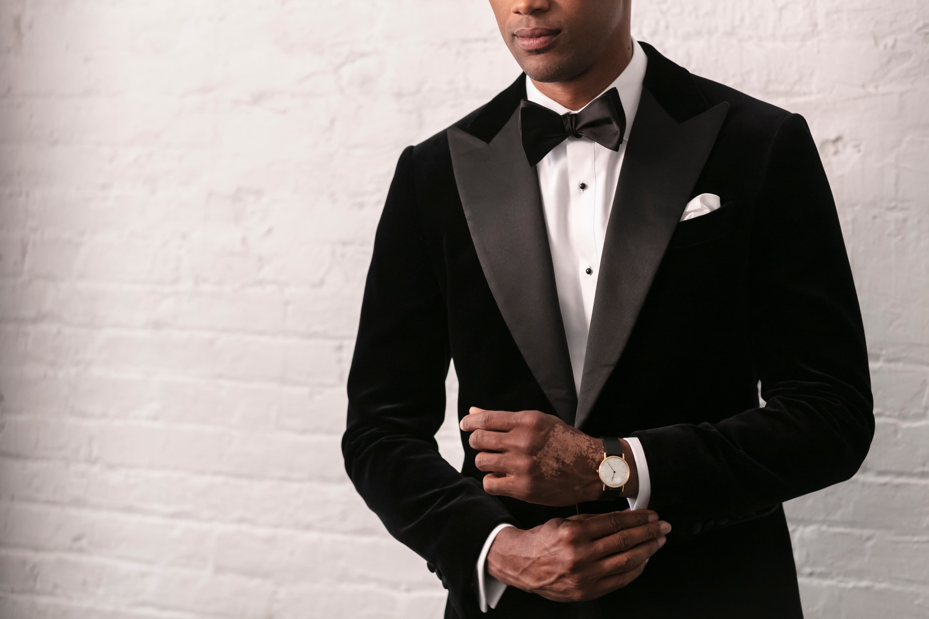 Groom in a black velvet tuxedo adjusting his cufflink